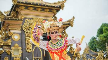 meisje vervelend balinees traditioneel jurk met een dansen gebaar Aan balinees tempel achtergrond met in de hand gehouden fan, kroon, sieraden, en goud ornament accessoires. balinees danser vrouw portret foto