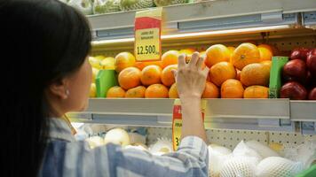 portret van een mooi Aziatisch of Indonesisch vrouw buying fruit geregeld Aan fruit rek in een supermarkt foto