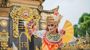 meisje vervelend balinees traditioneel jurk met een dansen gebaar Aan balinees tempel achtergrond met in de hand gehouden fan, kroon, sieraden, en goud ornament accessoires. balinees danser vrouw portret foto