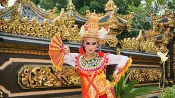 meisje vervelend balinees traditioneel jurk met een dansen gebaar Aan balinees tempel achtergrond met in de hand gehouden fan, kroon, sieraden, en goud ornament accessoires. balinees danser vrouw portret foto