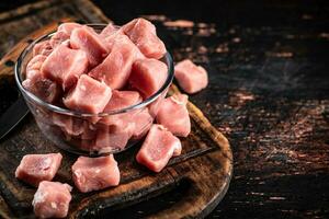 stukken van rauw varkensvlees in een kom Aan een snijdend bord. foto