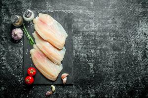 tilapia vis filet Aan een steen bord met tomaten, knoflook kruidnagel en specerijen. foto