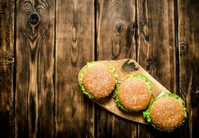 drie afgewerkt hamburger met vlees en groenten Aan houten stellage. foto