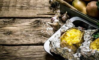 gebakken aardappelen in folie met zout en knoflook Aan een houten tafel . vrij ruimte voor tekst. foto