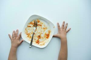 top visie van kind hand- en leeg bord na aan het eten Aan tafel foto