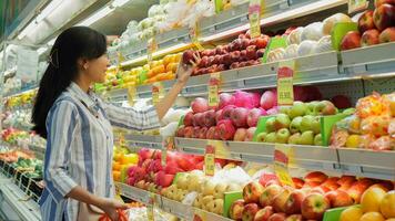 portret van een mooi Aziatisch of Indonesisch vrouw buying fruit geregeld Aan fruit rek in een supermarkt foto