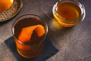 bruin boter whisky cocktail en oranje schil in een glas Aan de tafel foto