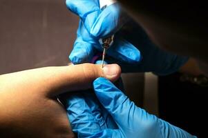 manicure in blauw handschoenen doet een hardware manicuren, mechanisch verwerken van nagels met een snijder, nagelriem verwijdering met een inrichting, professioneel manicure in een schoonheid salon. hand- zorg concept foto