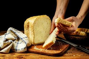 vrouw handen breken een stuk van vers wit eigengemaakt brood dat staat Aan een houten tafel. eigengemaakt taarten, gebakjes. foto