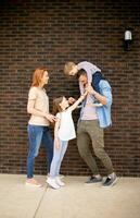 familie met een moeder, vader, zoon en dochter staand door de muur van steen huis foto