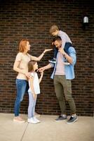 familie met een moeder, vader, zoon en dochter staand door de muur van steen huis foto