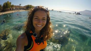 portret van gelukkig jong vrouw in wetsuit maken selfie Aan actie camera Bij de strand terwijl snorkelen. foto