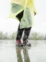 vrouw die in de regen speelt, in plassen springt met spatten foto