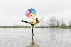 mooie donkerbruine vrouw die kleurrijke paraplu houdt die in de regen danst foto