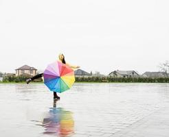 mooie donkerbruine vrouw die kleurrijke paraplu houdt die in de regen danst foto