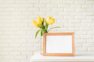 gele tulpen in een glazen vaas en blanco fotolijst foto