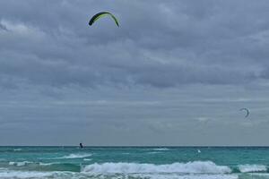 zomer landschap met de oceaan met donker bewolkt golven en surfermi uitrusting met parachutes drijvend Aan de kust foto