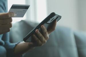 een credit kaart in de handen van een jong zakenvrouw pays voor een bedrijf Aan een mobiel telefoon en Aan een bureau met een laptop. foto