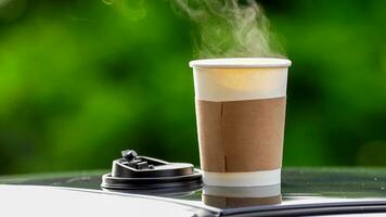 koffie meenemen in een papier kop Aan top van de auto dak groen boom achtergrond Bij zonsopkomst in de ochtend, selectief focus, zacht focus. foto