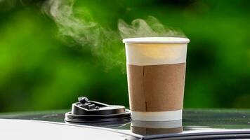 koffie meenemen in een papier kop Aan top van de auto dak groen boom achtergrond Bij zonsopkomst in de ochtend, selectief focus, zacht focus. foto