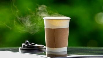 koffie meenemen in een papier kop Aan top van de auto dak groen boom achtergrond Bij zonsopkomst in de ochtend, selectief focus, zacht focus. foto