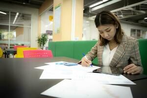 mooi Aziatisch zakenvrouw is zittend en scherpstellen Aan documenten in de bedrijf met vertrouwen. foto