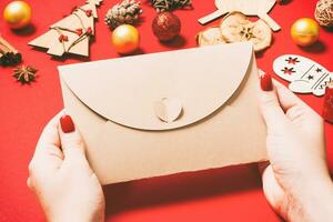 top visie van vrouw Holding een envelop Aan rood achtergrond gemaakt van vakantie decoraties. Kerstmis tijd concept foto