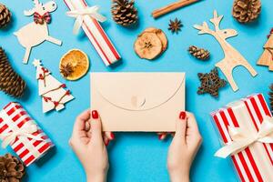 top visie van vrouw Holding een envelop Aan blauw achtergrond gemaakt van vakantie decoraties. Kerstmis tijd concept foto