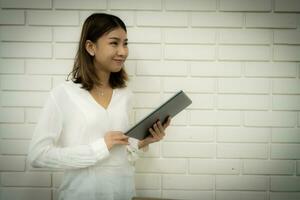mooi Aziatisch bedrijf vrouw heeft een idee naar ontwikkelen de bedrijf met haar idee terwijl staand en Holding tablet. foto
