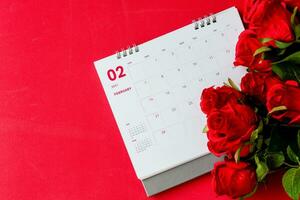 top visie, kalender van februari met wazig rood roos bloem Aan de rood achtergrond bureau, de concept voor Valentijnsdag dag Aan 14e februari 2021. detailopname, selectief focus, kopiëren ruimte voor ontwerp of tekst. foto