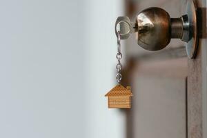 huis sleutel met huis sleutelhanger in de sleutelgat Aan de houten deur. de concept voor inkoop echt landgoed, bouw, huisvesting, condominium, kopen, en verkoop. foto