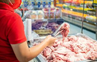 een vrouw houdt en looks Bij vers varkensvlees naar kopen kwaliteit stukken Bij de vers produceren sectie van de supermarkt. dichtbij omhoog, selectief focus, wazig achtergrond, kopiëren ruimte voor tekst of ontwerp. foto