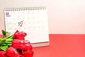 de concept voor Valentijnsdag dag Aan 14e februari 2022. Mark hart Aan 14e kalender van februari met rood tulpen bloem Aan de rood achtergrond Aan een bureau, kopiëren ruimte, selectief focus, wazig achtergrond foto