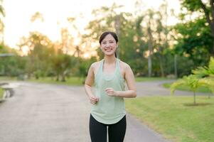 fit Aziatisch jong vrouw jogging in park glimlachen gelukkig rennen en genieten van een gezond buitenshuis levensstijl. vrouw jogger. geschiktheid loper meisje in openbaar park. gezond levensstijl en welzijn wezen concept foto