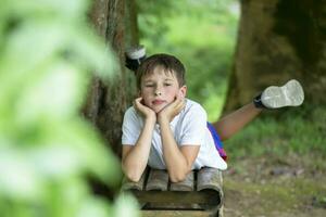 een knap jong jongen leugens Aan een bank in de achtergrond van een zomer tuin. foto