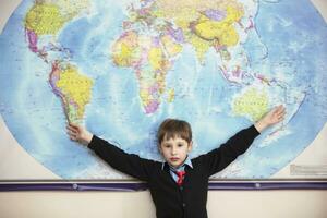 de kind staat Bij de geografisch kaart van de wereld. elementair school- leerling glimlacht Bij de kaart van de wereld. foto