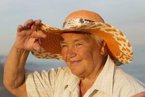 mooi ouderen vrouw in een hoed Aan de achtergrond van de zee. gezicht van een oud vrouw met een glimlach. grootmoeder Aan vakantie foto