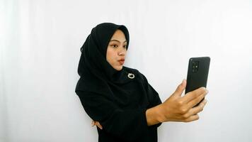 vrolijk jong Aziatisch vrouw nemen selfie, kijken smartphone voorkant camera geïsoleerd over- wit achtergrond foto