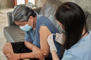 een aziatische vrouwelijke arts vaccineert thuis een oudere man.