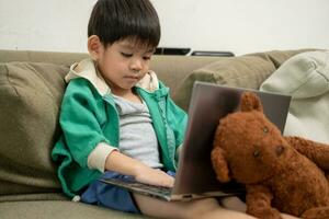 Aziatisch jongen aan het studeren online en aan het doen activiteiten Aan laptop foto