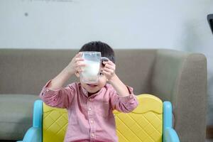 Aziatisch jongen is drinken een glas van melk foto