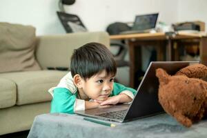 Aziatisch jongen aan het studeren online en aan het doen activiteiten Aan laptop foto
