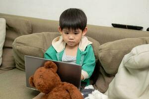 Aziatisch jongen aan het studeren online en aan het doen activiteiten Aan laptop foto