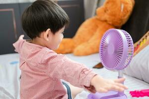 Aziatisch jongen aan het liegen Aan de matras Aan een heet dag spelen met een portable ventilator gelukkig foto