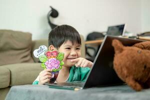 Aziatisch jongen aan het studeren online en aan het doen activiteiten Aan laptop foto