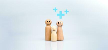 de concept van Gezondheid verzekering en medisch welzijn. een familie van houten poppen met een plus teken Aan een wit achtergrond vertegenwoordigt bescherming, ontvangen een uitkering. Gezondheid zorg planning foto