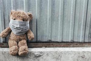 teddybeer met medisch masker zit in de buurt van metalen hek. foto