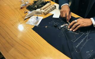kleermaker handen met schaar, draad, en zwart kleding stof Aan gepolijst werkbank foto