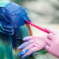 kant visie van werkwijze van verven haar- in elegant kleur. kapper in roze handschoen gebruik makend van magenta borstel terwijl toepassen blauw verf naar haar- foto