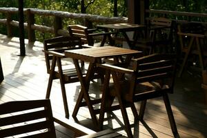 houten tafels en stoelen Bij buitenshuis cafe terras in park. leeg tuin meubilair omringd door groen tuin. foto